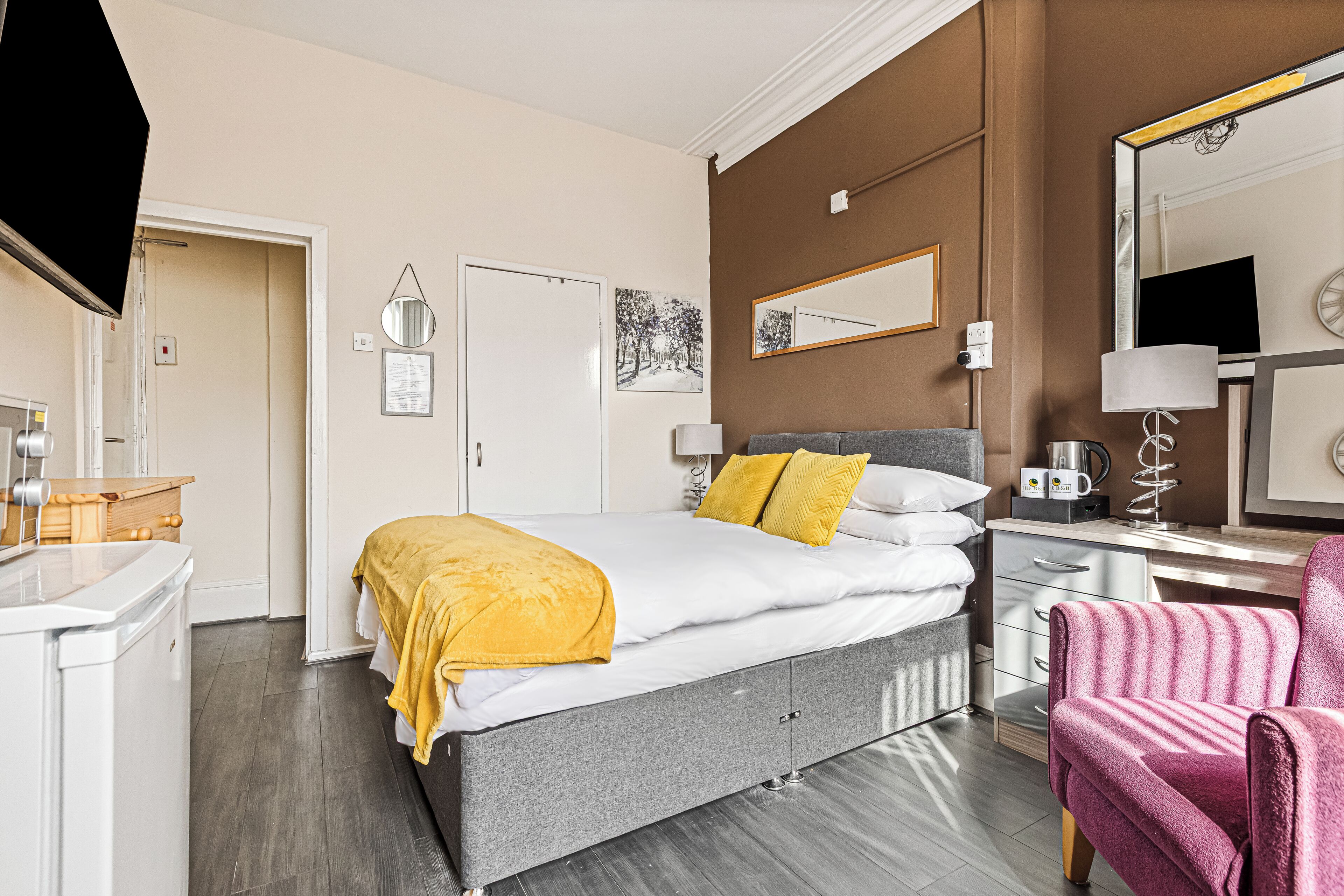 A hotel room with a bed, bedside table, chair, desk, and a mirror.