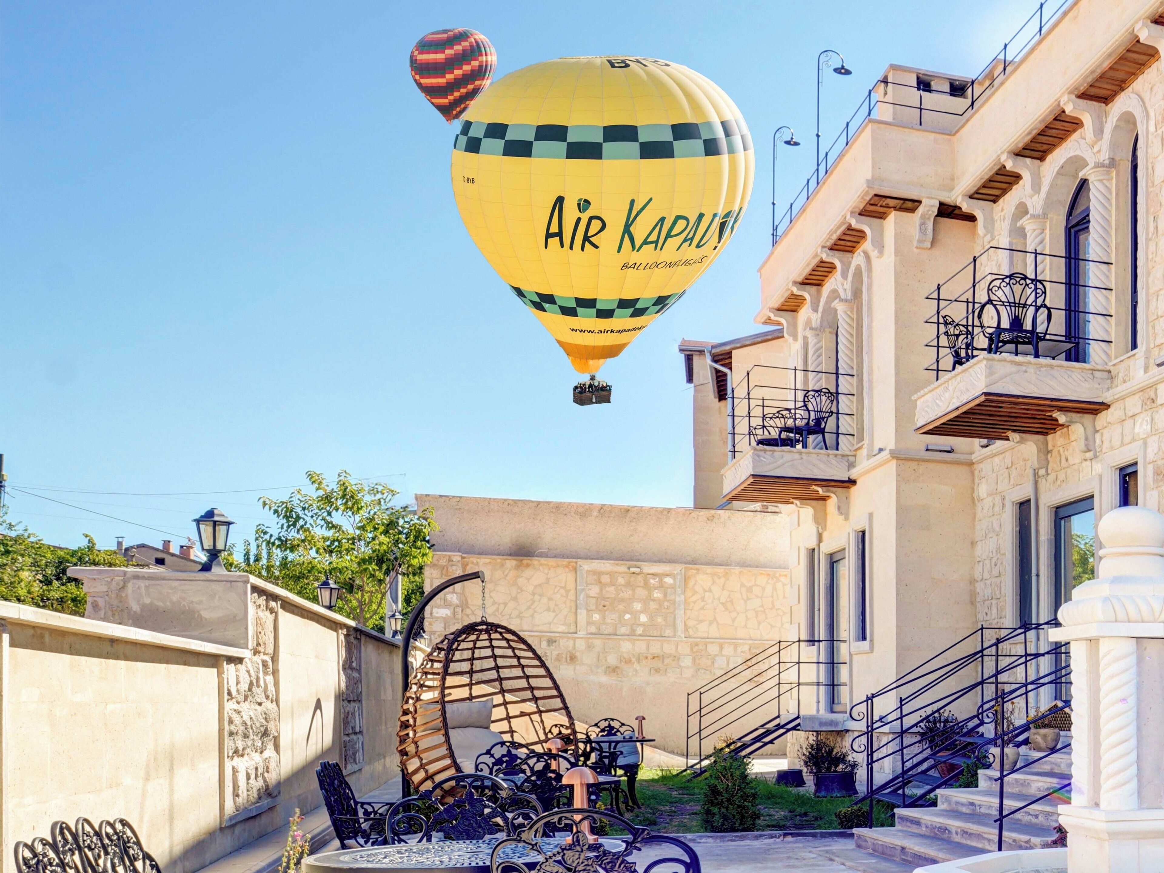 Eine gelbe Heißluftballon mit dem Aufdruck "Air Kapalou", ein Steinhaus mit Balkon und ein Hängekorbstuhl.