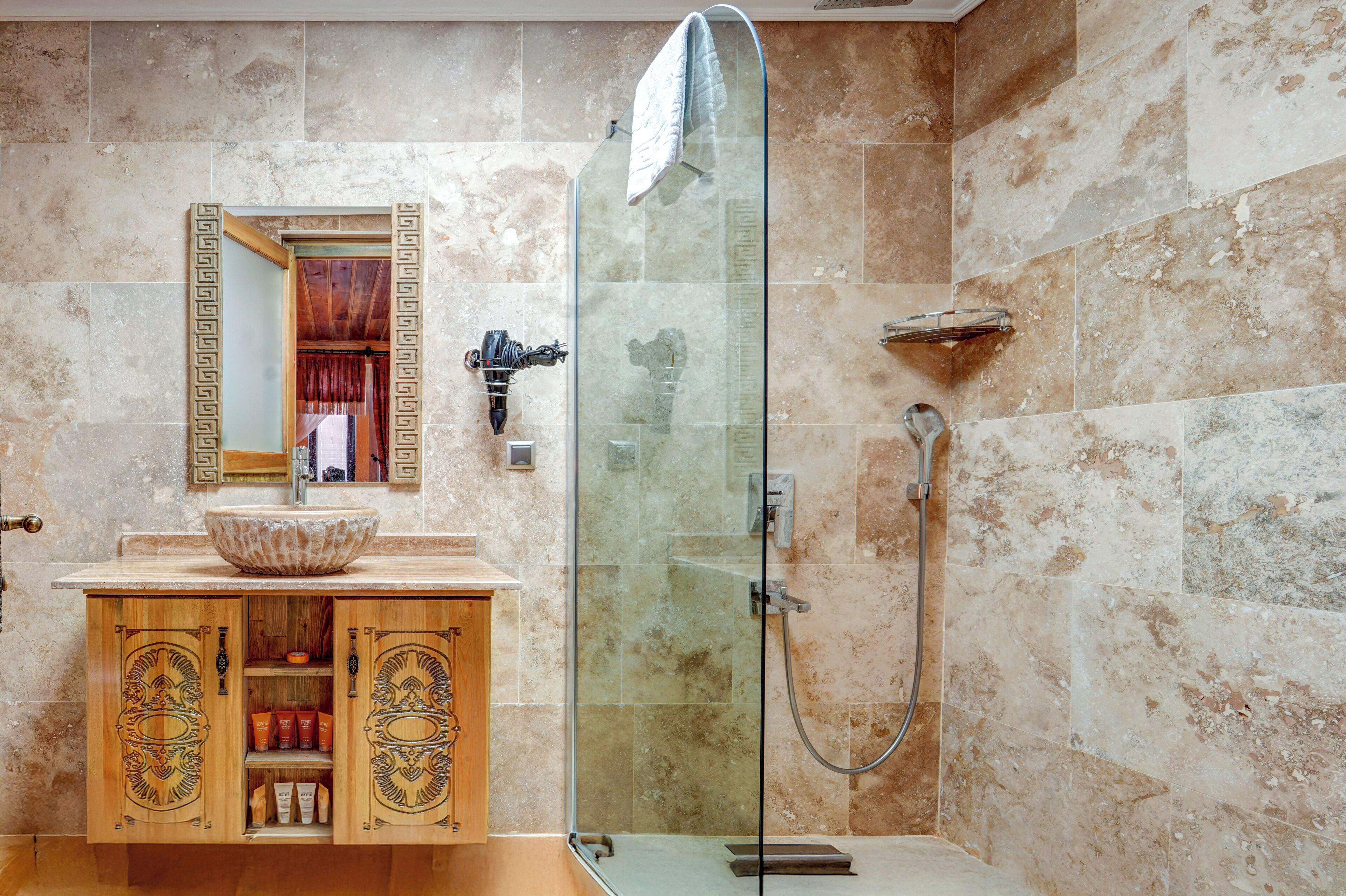 Un baño con ducha envuelta en vidrio, un tocador de madera con lavabo y un espejo con marco decorativo.