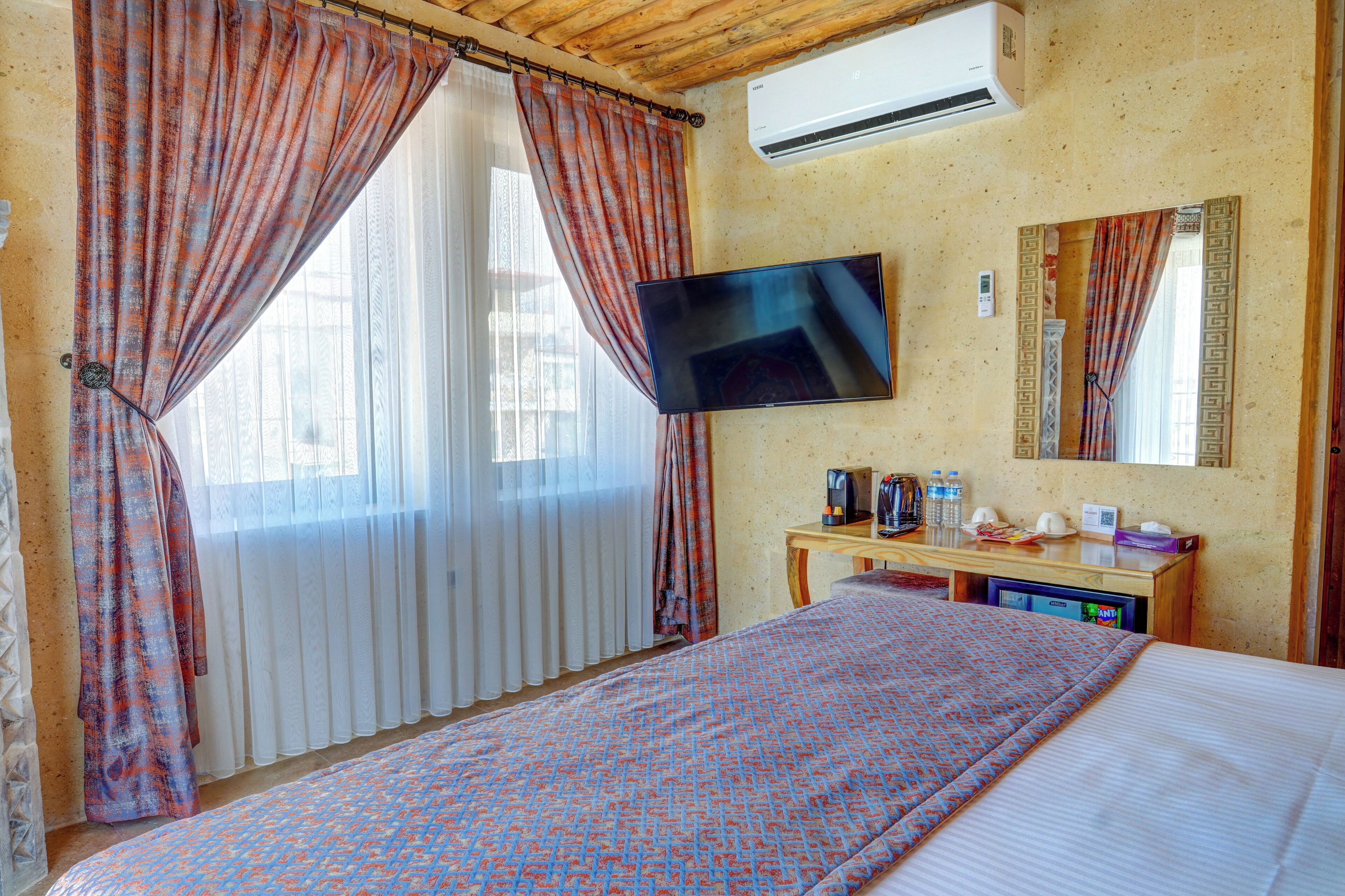 A hotel room with a bed, a flat-screen TV, a wooden desk with a coffee maker, and a mirror on the wall.