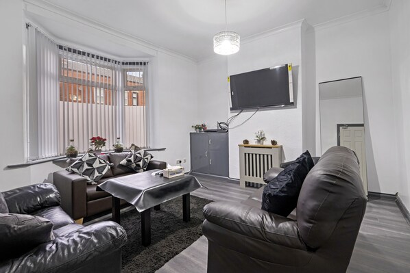 A modern living room with a sofa, a coffee table, and a TV mounted on the wall. - Stunning 5bed House in Birmingham Contractors Also (Birmingham)