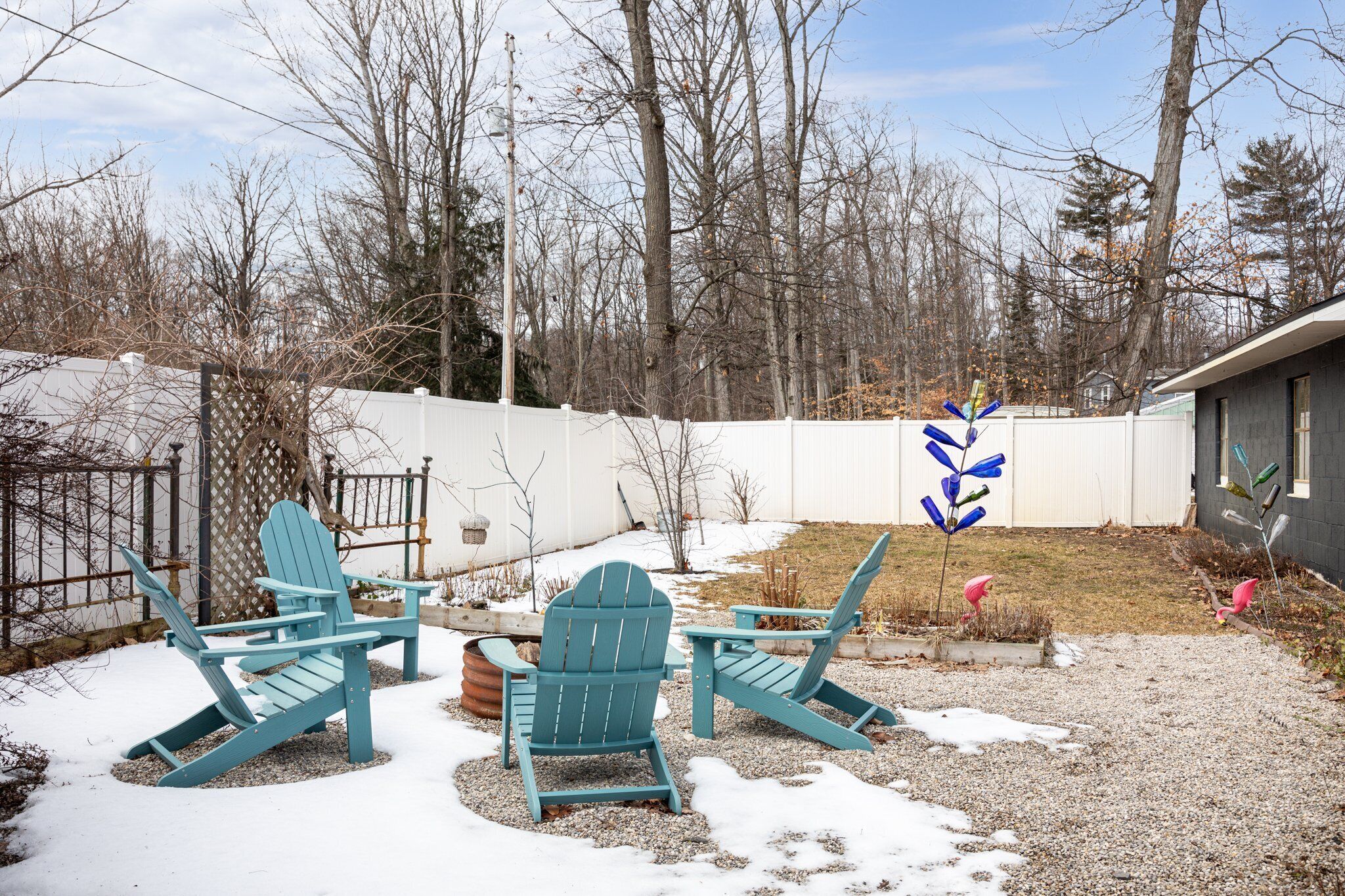 A backyard with two Adirondack chairs, a wooden fence, and a gravel path.