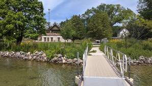 Eine Holzbrücke über einen Teich, an einer Seite eine Steinmauer und im Hintergrund ein Gebäude mit schrägem Dach.
