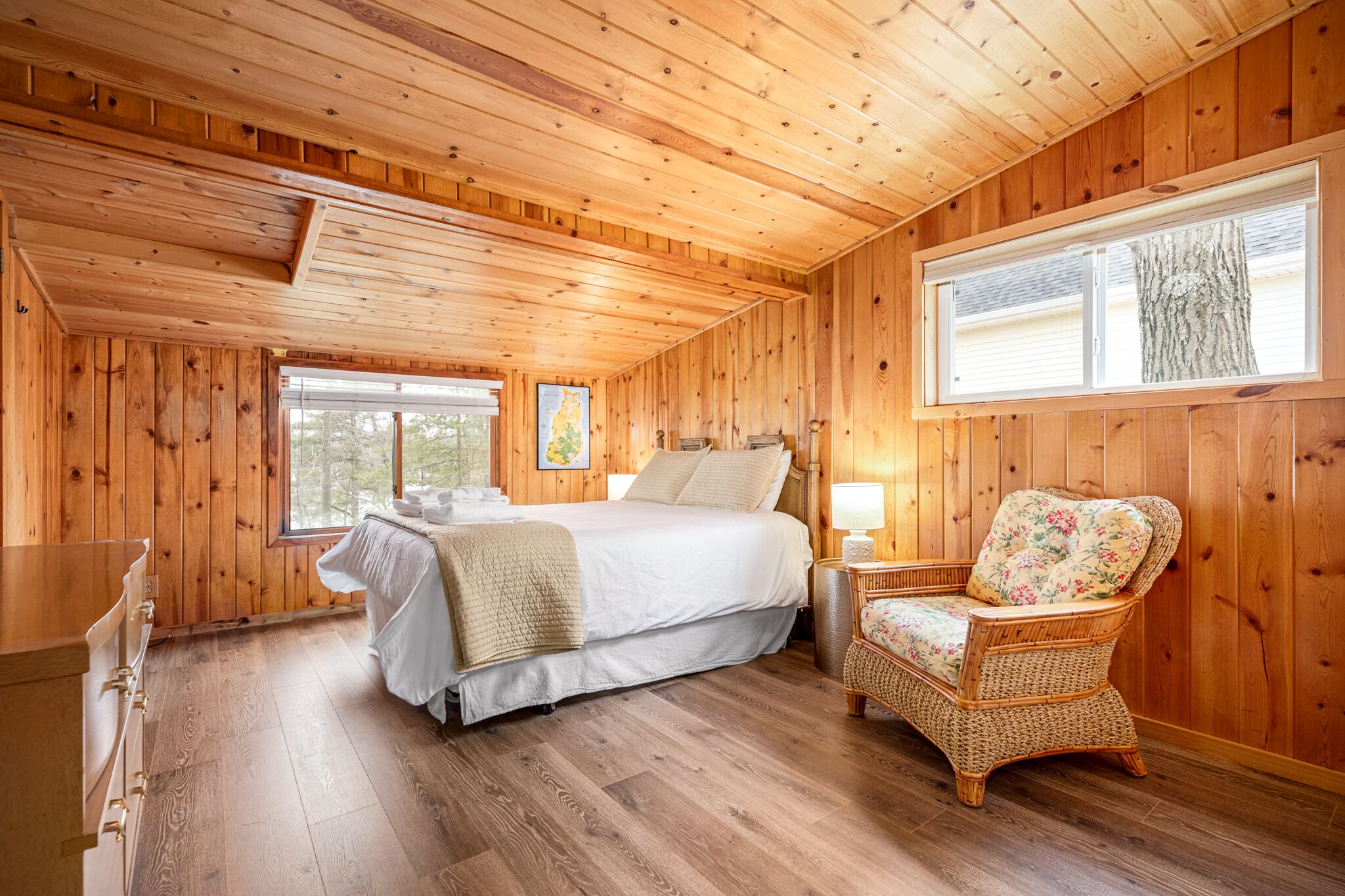 A wooden cabin bedroom with a bed, a chair, a window, and a dresser.