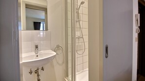 Un baño con lavamanos blanco, espejo y cabina de ducha.