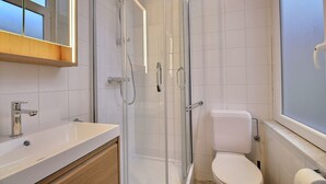 Moderni kylpyhuone, jossa on lasiseinällä varustettu suihku, valkoinen pesuallas ja wc.