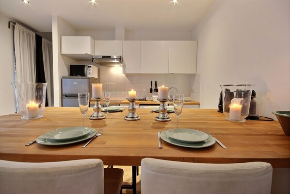 A dining area with a wooden table set for four, surrounded by white chairs.