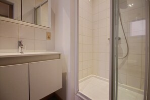Un baño con ducha de vidrio, un lavabo blanco y un espejo sobre el lavabo.