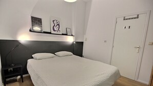 A bedroom with a bed, bedside table, lamp, and wall-mounted shelf with framed pictures. - Li Tore 1 - Nice practical studio in the center (Liège)