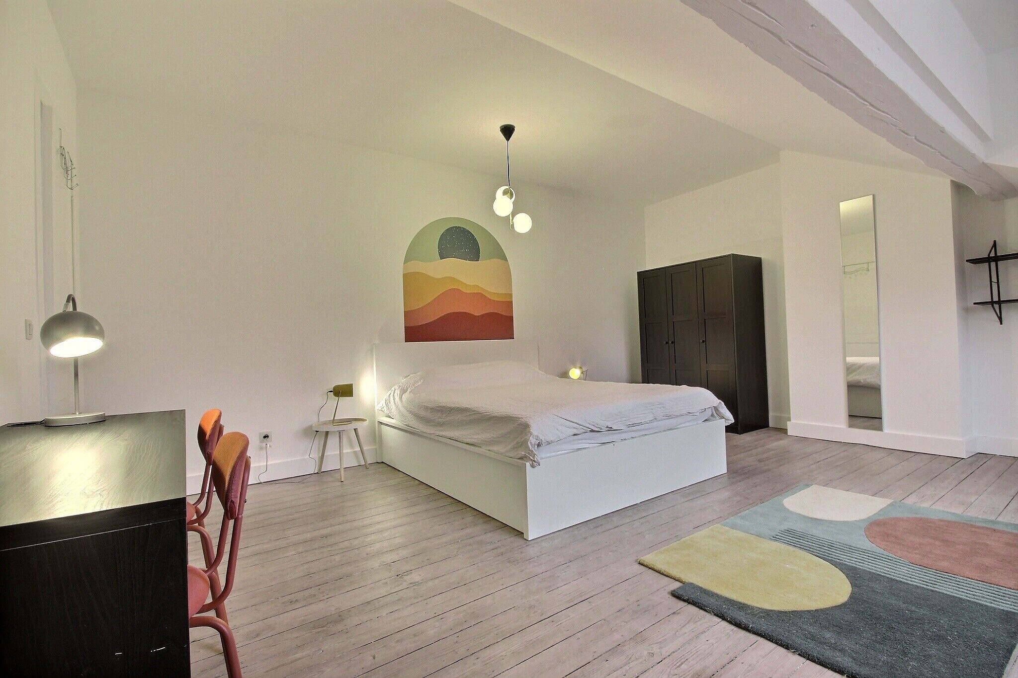A bedroom with a bed, a desk, a chair, a wardrobe, and a painting on the wall.