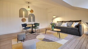 A modern living room with a sofa, coffee table, and chairs. There is a dining table with chairs and a decorative wall piece.