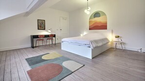 A bedroom with a bed, a desk, two chairs, and a colorful abstract painting on the wall.