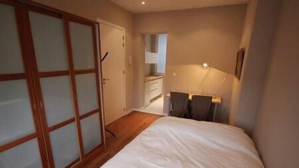 Ein Schlafzimmer mit Bett, Schreibtisch und Stuhl. Ein Kleiderschrank mit Milchglas-Türen und eine Tür zu einem Badezimmer.