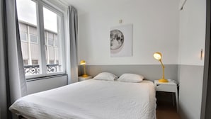 Ein Schlafzimmer mit einem Bett, zwei Nachttischen mit Lampen, einem Fenster mit Vorhängen und einem an der Wand hängenden Bild.