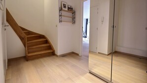 A modern interior with a wooden staircase, a glass door, and a white wall with a shelf. - Chez Rémy - 3 bedrooms (Liège)