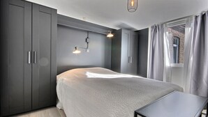 A modern bedroom with a large bed, grey wardrobe, and a small table. - Chez Rémy - 3 bedrooms (Liège)