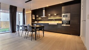 A modern kitchen with dark cabinetry, stainless steel appliances, and a dining area with a table and chairs. - Chez Rémy - 3 bedrooms (Liège)