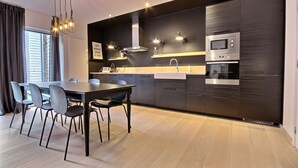 A modern kitchen with dark cabinetry, a stainless steel oven, and a dining area with a table and chairs. - Chez Rémy - 3 bedrooms (Liège)