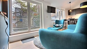 A modern living room with large windows, a flat-screen TV, and teal furniture. - Li Tore 3 - Pretty modern studio in the center (Liège)