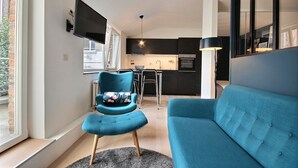 A modern kitchen with dark cabinetry, a dining area with a table and chairs, and a blue sofa in a living area with a large window. - Li Tore 3 - Pretty modern studio in the center (Liège)