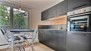 A modern kitchen with dark cabinetry, a built-in oven, and a dining area with foldable chairs. - Li Tore 3 - Pretty modern studio in the center (Liège)