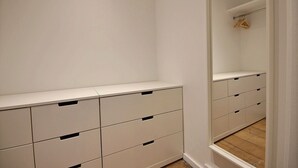 Een smalle gang met een witte garderobe met meerdere lades en een spiegel.