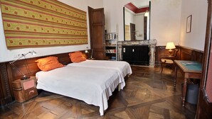 A bedroom with a large bed, a wooden floor, a fireplace, and a bookshelf.