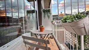 Un balcon avec une table, des chaises, des plantes suspendues et un cactus en pot.