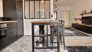 Une cuisine moderne avec des meubles de couleur sombre, une table à manger en bois et des luminaires suspendus.