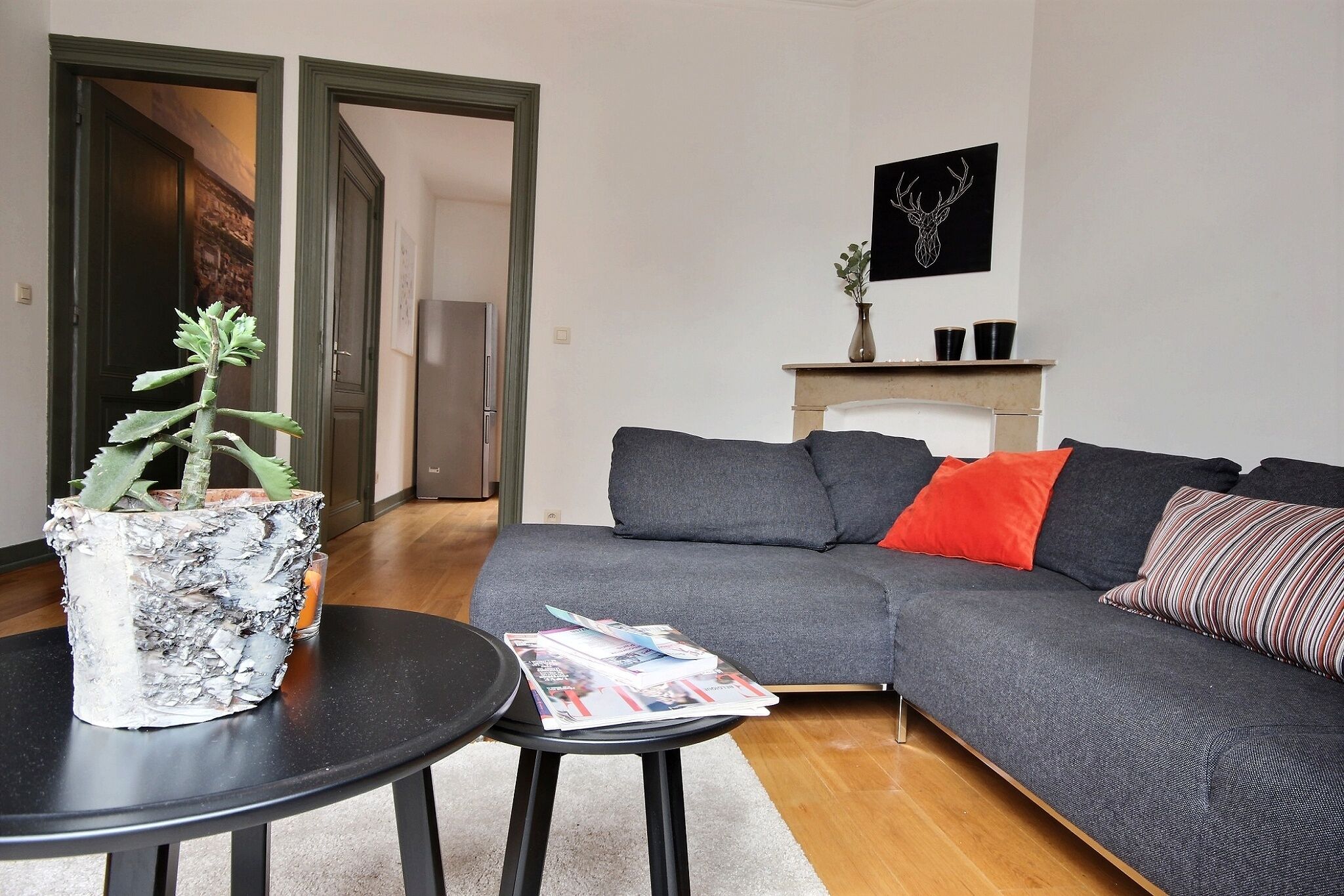 Una sala de estar con un sofá gris, una mesita con una planta en maceta y una chimenea decorada.
