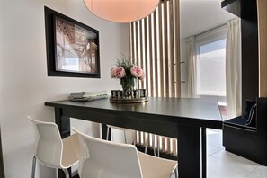 A modern dining area with a dark table, white chairs, a vase with flowers, and a framed picture on the wall. - Plan 75  - 1 bedroom (Liège)