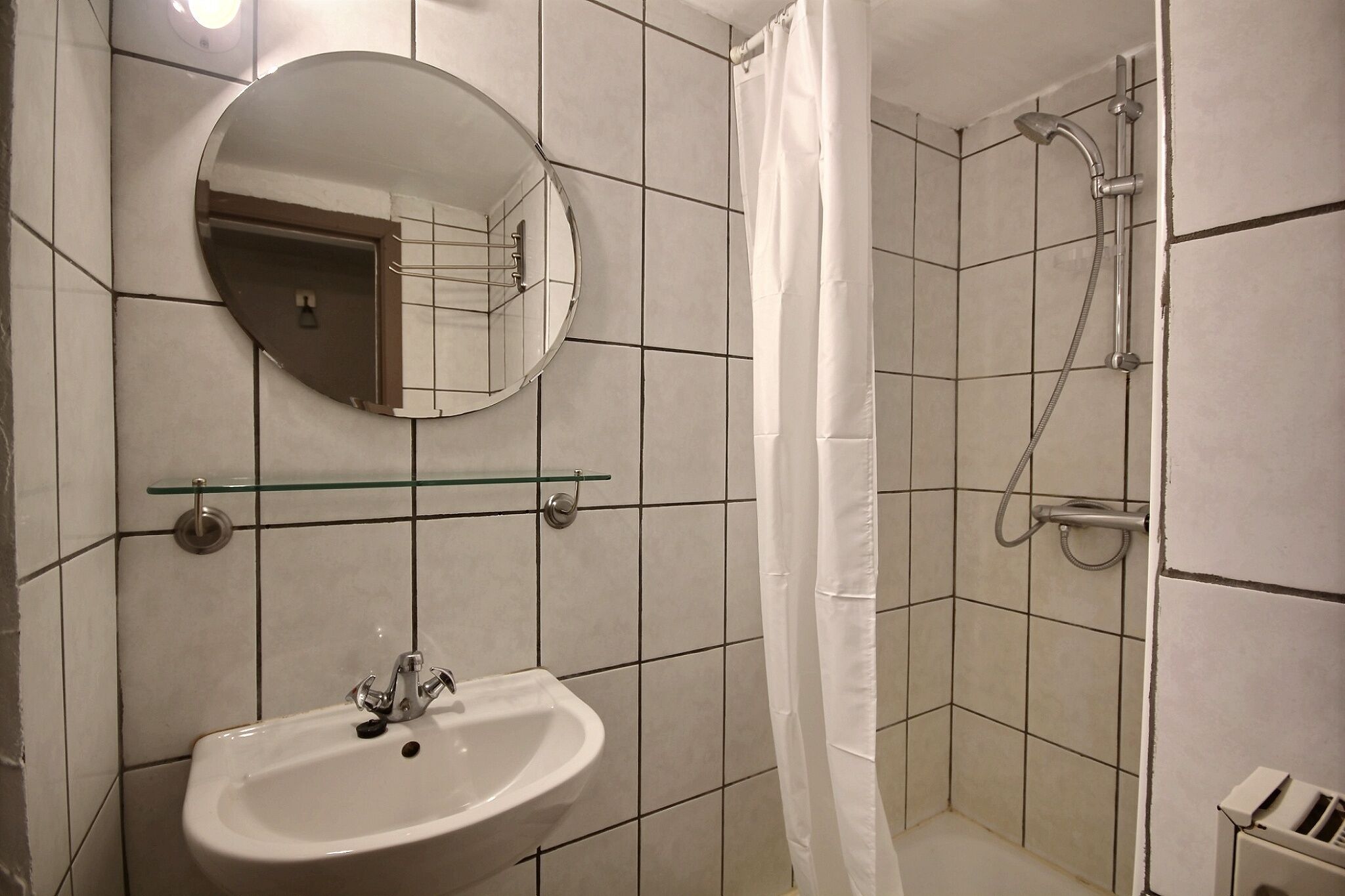 Une salle de bain avec un lavabo, un miroir rond, une étagère en verre et une douche.