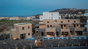 A modern hotel with multiple buildings, a swimming pool, and a view of the sea and hills. - Hidden Hills (Santorini)