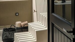 A room with a large window offering a view of a mountainous landscape. There is a black woven basket with towels on the windowsill. - Hidden Hills (Santorini)