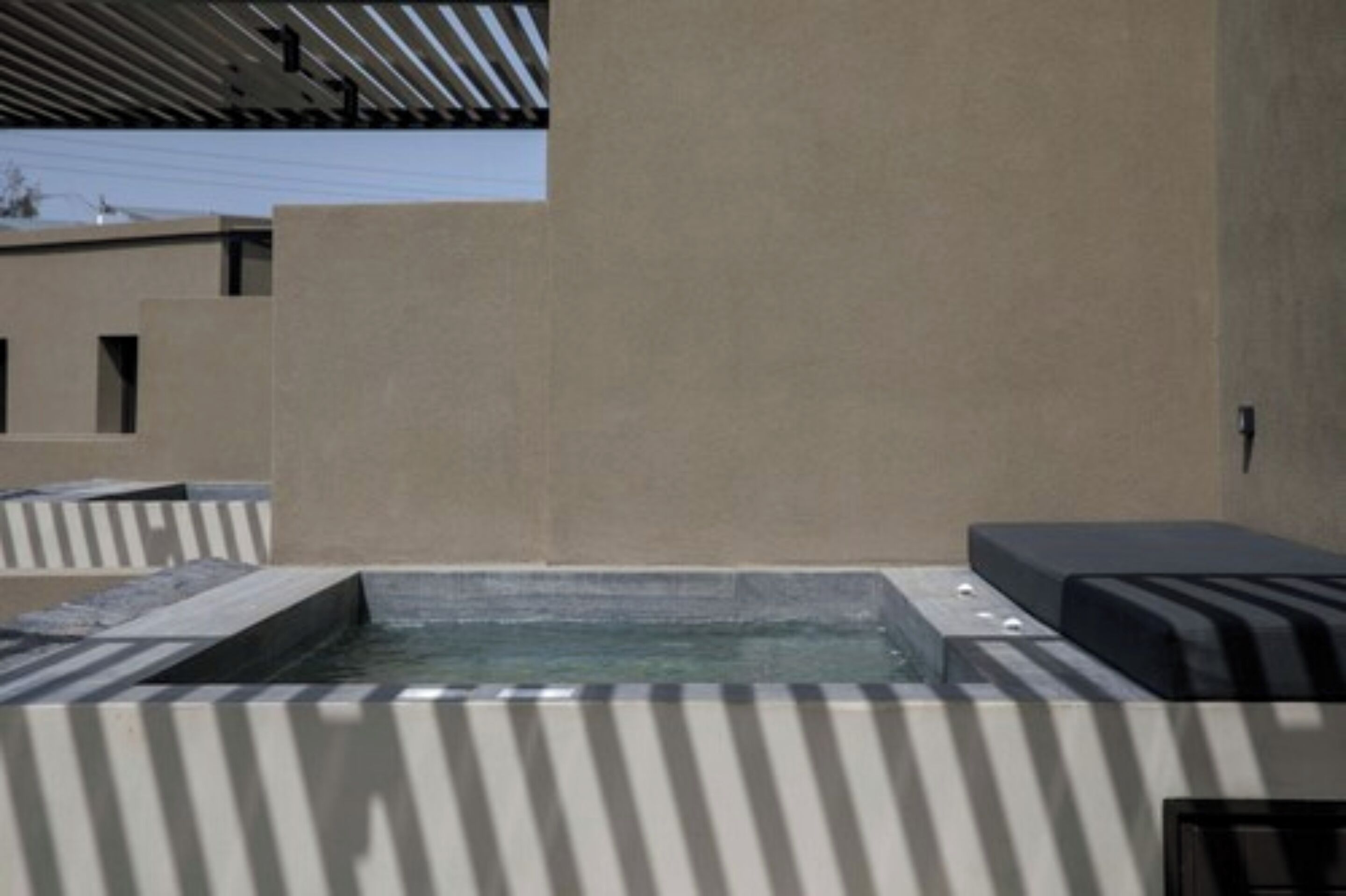 A modern outdoor relaxation area with a hot tub, seating, and a sloped roof structure.