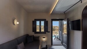 A modern interior with a sofa, a table, a wall-mounted TV, and a door leading to an outdoor area. - Hidden Hills (Santorini)