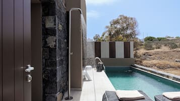 Uma área de piscina moderna com muro de pedra, fonte de água e cadeiras de lounge com toalhas.