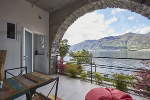 Un balcón con arco de piedra, una mesa, sillas y vistas a un lago y montañas.