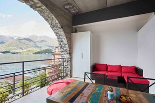 Un balcón con un arco de piedra, un sofá rojo y una mesa de madera con una planta.