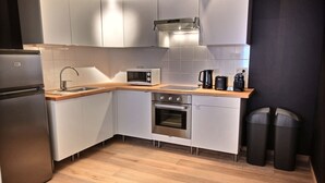Una cocina moderna con armarios blancos, un refrigerador de acero inoxidable, un microondas, un horno y una cafetera.