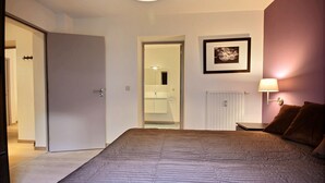 Un dormitorio con cama, mesita de noche, lámpara, un cuadro enmarcado y una puerta que da al baño.