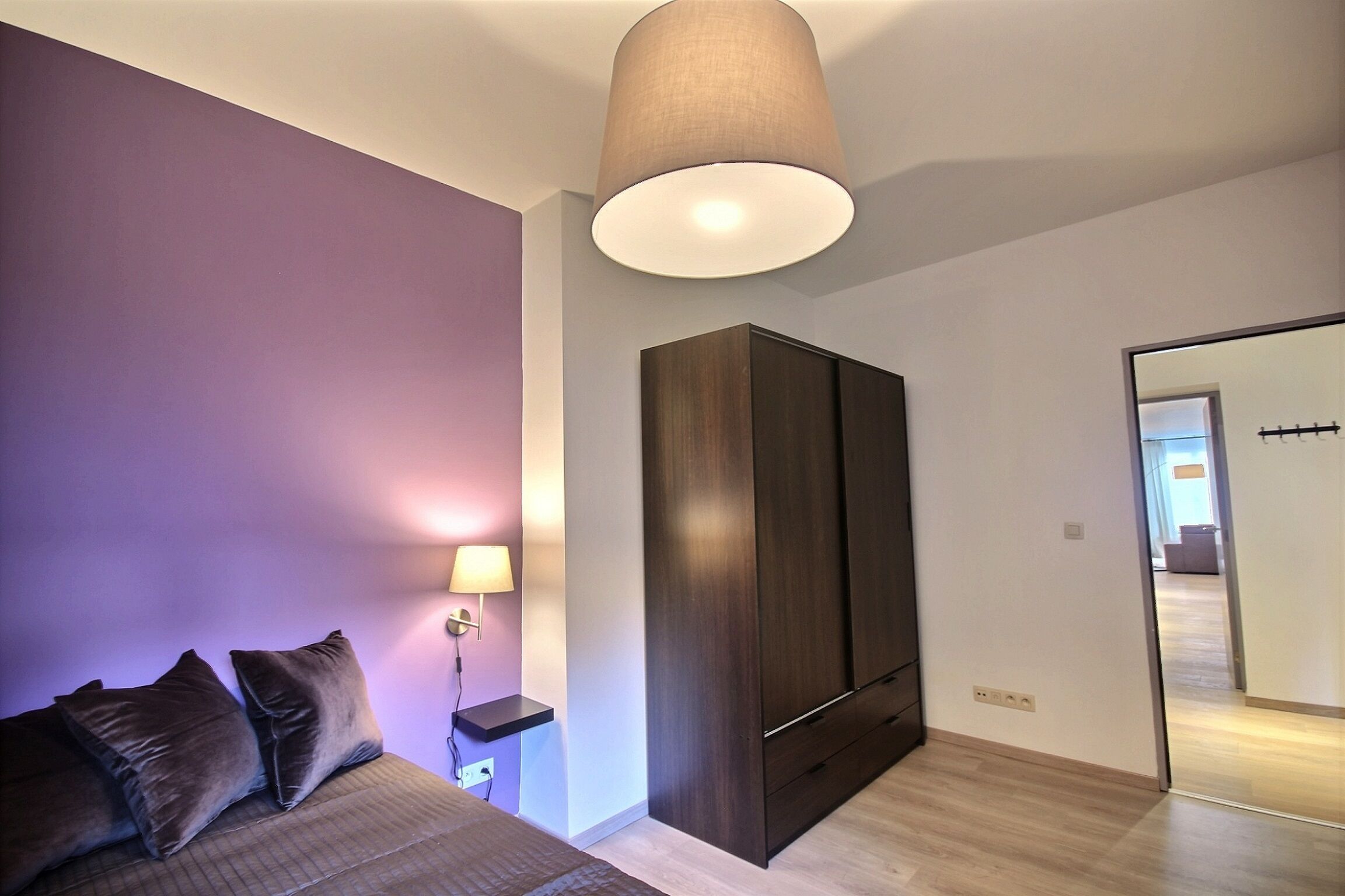 Une chambre à coucher avec un lit, une armoire, une table de chevet avec une lampe et un miroir.