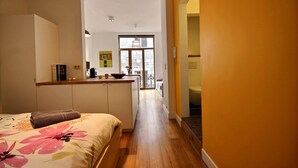 A narrow, well-lit hallway with a bed on the left and a kitchen area on the right. - Goffe Street - Studio (Liège)