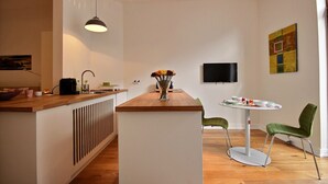 A modern kitchen with a wooden countertop, a vase with flowers, a round dining table with green chairs, and a flat-screen TV mounted on the wall. - Goffe Street - Studio (Liège)