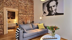 Un salon moderne avec un mur en briques, un canapé gris, une petite table sur laquelle est posé un vase de fleurs et un tableau accroché au mur.
