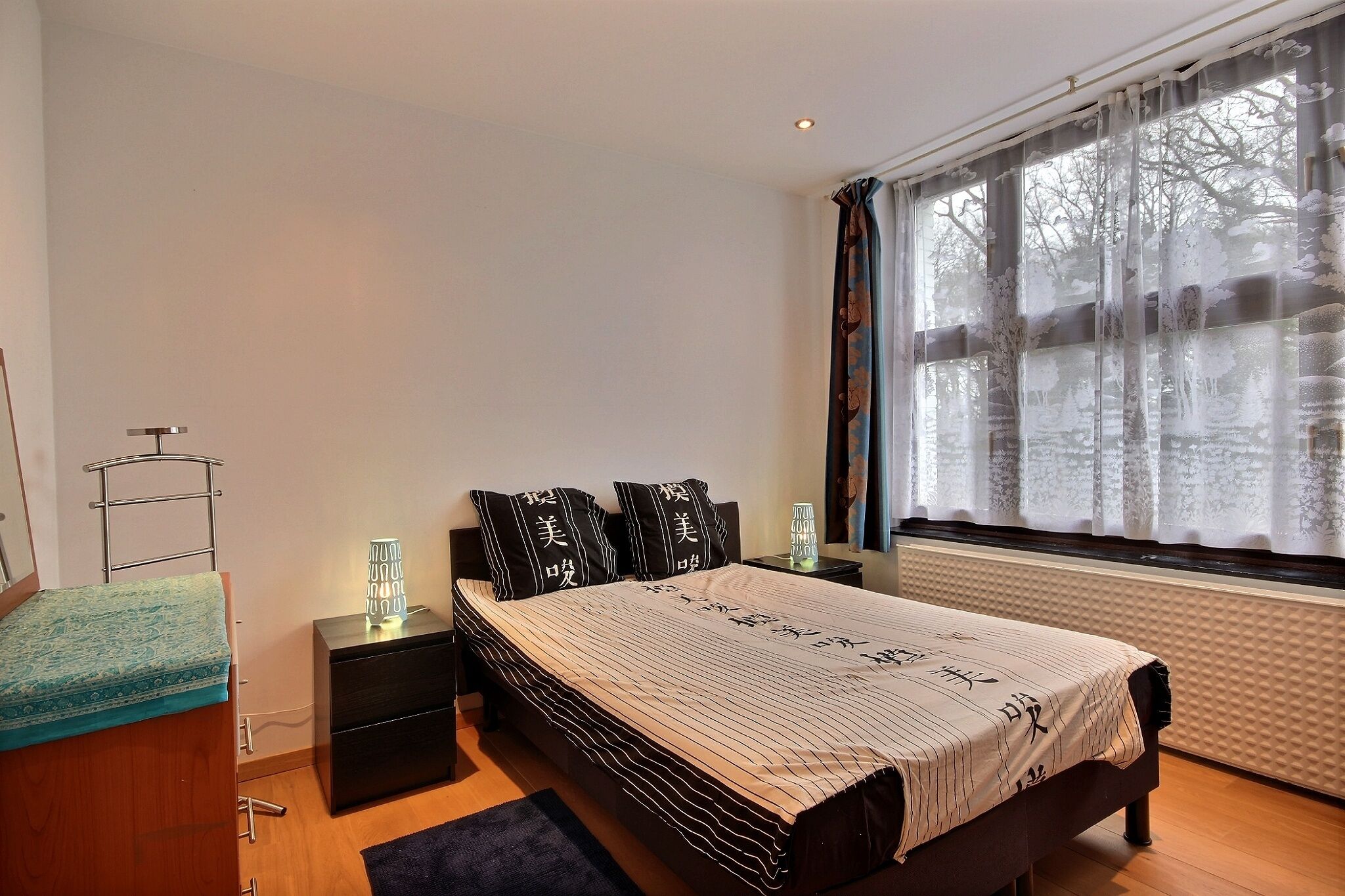 A bedroom with a bed, bedside tables, a nightstand, a dresser, and a window with curtains.