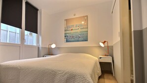 Une chambre à coucher avec un lit, deux tables de chevet, un tableau au mur et une fenêtre avec des stores.