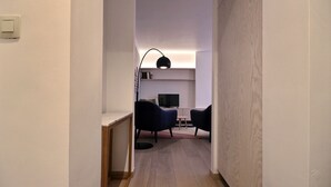 Un couloir étroit avec un bureau, deux chaises, une petite table et un téléviseur.