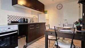 Una cocina moderna con armarios oscuros, un refrigerador blanco y un comedor con una mesa dispuesta para dos.