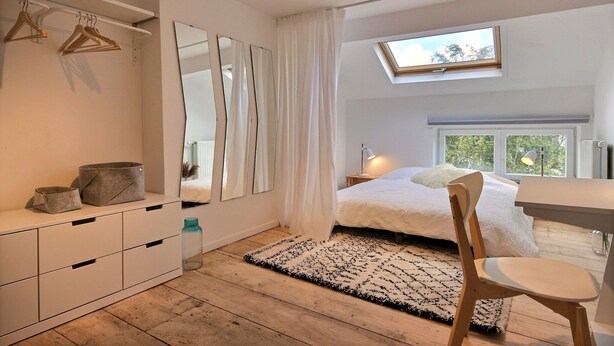 Un dormitorio con cama, escritorio, silla, armario y tragaluz.